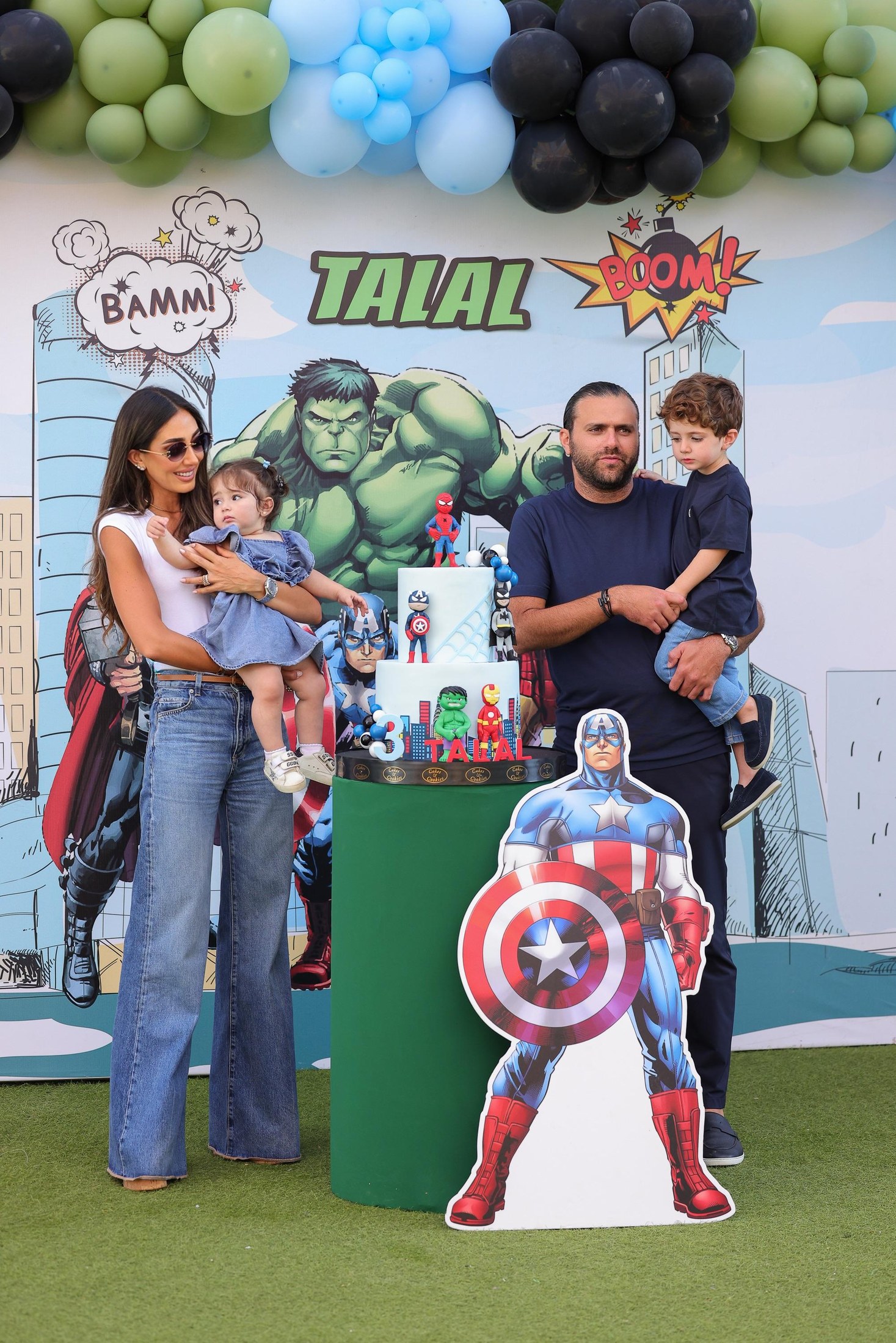 Family posing at a Recreo birthday setup with balloons and superhero artwork